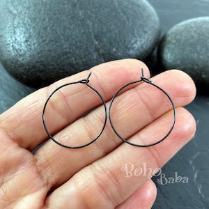 May include: A pair of black hoop earrings. The earrings are thin and delicate, and they are made of metal.