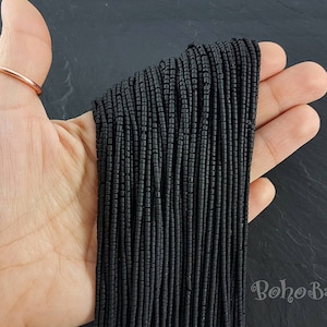 May include: A close-up of a hand holding a bundle of black seed beads. The beads are small and round, and they are arranged in a neat stack. The beads are ideal for jewellery making or other craft projects.