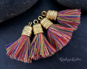 May include: Four colorful tassel ornaments with gold metal tops. The tassels are made of multi-colored yarn and have a fringe-like appearance. The gold tops have a decorative design.