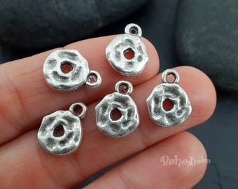Peut inclure: Gros plan sur plusieurs petits charms en métal argenté. Chaque charm a une forme de donut avec un trou central et une surface texturée. Une petite boucle est attachée en haut pour l'enfilage. Les charms sont probablement destinés à la fabrication de bijoux ou à l'artisanat.