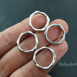 Puede incluir: Cuatro anillos de plata con un acabado texturizado martillado. Los anillos son todos del mismo tamaño y forma, y están dispuestos en un círculo.