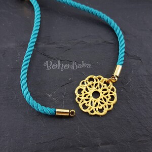 May include: A turquoise cord necklace with a gold filigree pendant. The pendant is a circular design with a small hole in the center.