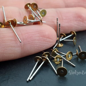 Puede incluir: Primer plano de un mont&oacute;n de postes de pendientes de color dorado con tallos plateados. Los postes de pendientes est&aacute;n esparcidos sobre una superficie oscura.