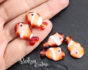 May include: Five orange and white glass fish beads with black eyes. The beads are approximately 1 inch long and have a red tail fin.