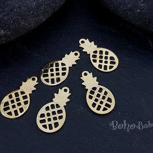 May include: Five gold metal pineapple charms with a cutout design. The charms are on a black background.