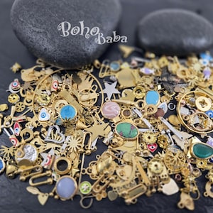 May include: A collection of gold-toned charms and pendants, including stars, crowns, and various shapes, with colorful gemstone accents. The text "Boho Baba" is visible in the upper center. Ideal for jewelry making and crafting.
