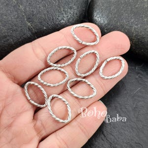 May include: Silver oval jump rings with a twisted wire design. The rings are approximately 1 inch in diameter.
