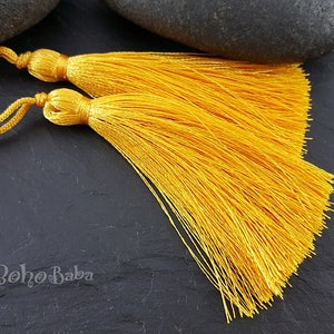 May include: Two bright yellow tassels with a cord attached. The tassels are made of soft, silky threads and are approximately 2 inches long.