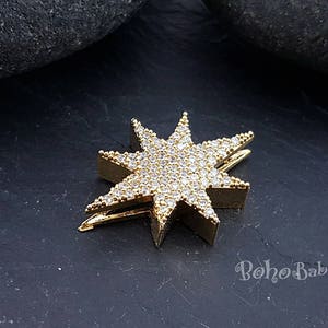 Puede incluir: Pinza para el pelo en forma de estrella dorada con diamantes de imitaci&oacute;n transparentes. La pinza est&aacute; sobre una superficie gris oscura.