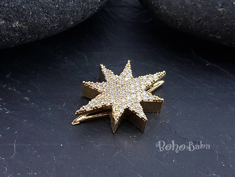 Puede incluir: Pinza para el pelo en forma de estrella dorada con diamantes de imitaci&oacute;n transparentes. La pinza est&aacute; sobre una superficie gris oscura.