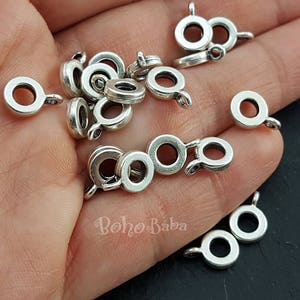 Może przedstawiać: Zbliżenie na kolekcję srebrnych metalowych kółek do łączenia. Kółka są różnych rozmiarów i ułożone są w stos na dłoni.