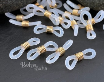 May include: A close-up of a group of white plastic eyeglass chain connectors with gold metal accents. The connectors are arranged on a dark gray surface.