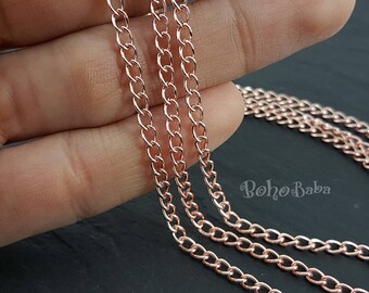 May include: Three strands of rose gold chain, each with a different size link, are draped over a hand. The chains are all connected together at the top.