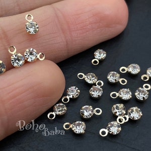 May include: A collection of 15 gold-toned metal charms with clear crystal rhinestones. Each charm has a loop on top for attaching to jewellery or other crafts.