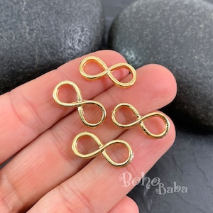 Può includere: Quattro ciondoli dorati a forma di simbolo di infinito. I ciondoli sono piccoli e delicati, perfetti per aggiungere un tocco di eleganza a gioielli o artigianato.