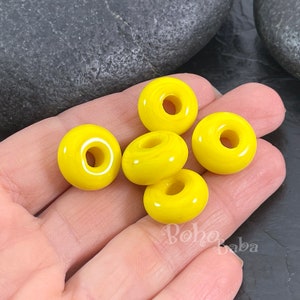 Puede incluir: Cinco cuentas de cerámica de color amarillo brillante en forma de rosquilla con un agujero en el centro. Las cuentas son lisas y brillantes.