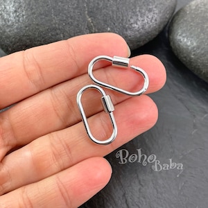 以下が含まれることがあります： 2つの銀色の金属製のロブスタークラスプが、片方の手の上に置かれています。クラスプは楕円形で、バネ式のメカニズムになっています。