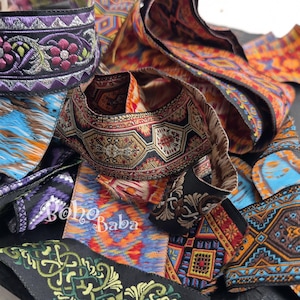 May include: A collection of colorful, patterned ribbons and trims. The ribbons feature various designs, including floral, geometric, and abstract patterns in shades of purple, blue, orange, and black. The text "Boho Baba" is visible.