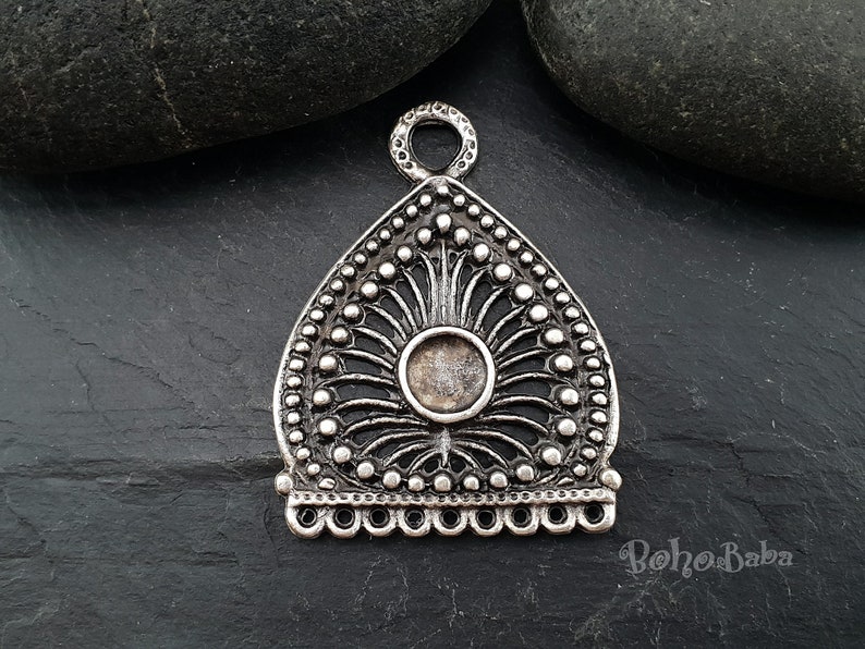 Pu&ograve; includere: Ciondolo in argento con un design decorativo e ornato. Il ciondolo ha un'apertura circolare al centro e un anello in alto per appenderlo.