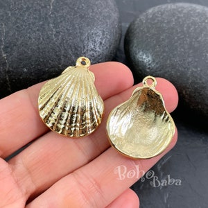 Könnte beinhalten: Zwei goldfarbene Muschel-Anhänger aus Metall. Die Muscheln sind detailliert und haben eine strukturierte Oberfläche. Die Anhänger haben oben ein Loch zum Anbringen an Schmuck oder anderen Bastelarbeiten.