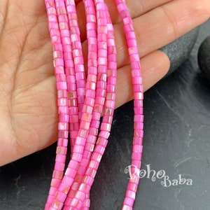 Puede incluir: Una hebra de cuentas cuadradas de concha rosa. Las cuentas tienen un ligero brillo iridiscente. Las cuentas están enhebradas en un hilo transparente.