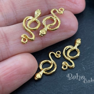 Puede incluir: Cuatro colgantes de serpiente de color dorado. Los colgantes de serpiente están enroscados en forma de círculo con una cola que forma un bucle. Los colgantes son perfectos para la elaboración de joyas o para agregar un toque único a las manualidades.