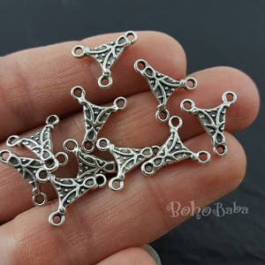 Pode incluir: Conectores de joias em metal prateado com formato triangular e detalhes ornamentados. Cada conector possui três laços para fixação. Os conectores são exibidos em um fundo neutro.