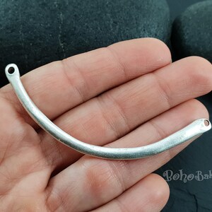 May include: Silver-toned metal connector with two holes, shaped like a curved bar. The connector is approximately 2 inches long.