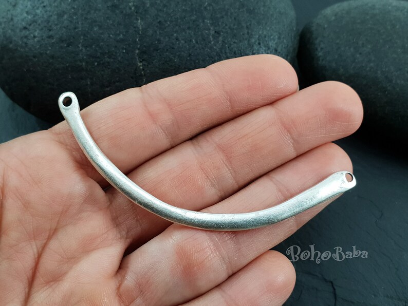 May include: Silver-toned metal connector with two holes, shaped like a curved bar. The connector is approximately 2 inches long.