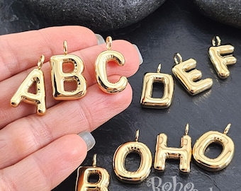 Könnte beinhalten: Goldfarbene Metall-Anhänger in Form von Buchstaben des Alphabets. Die Buchstaben sind in einem prallen, ballonartigen Stil gehalten. Die gezeigten Buchstaben sind A, B, C, D, E, F, O und H.