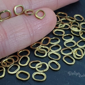 Peut inclure: Une collection de petits anneaux ovales dorés. Certains anneaux sont ouverts, d'autres sont fermés. Les anneaux sont dispersés sur une surface sombre, certains étant tenus dans une main. L'image est bien éclairée, soulignant l'éclat métallique des anneaux.