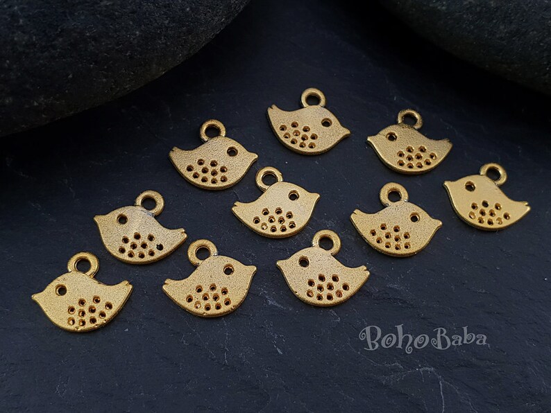 May include: A collection of ten gold-colored metal bird charms with a dotted pattern. The charms have a loop at the top for attaching to jewelry or other crafts.