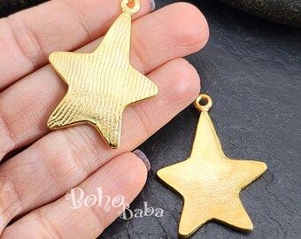 May include: Two gold-tone metal star-shaped charms with a textured surface. The charms are approximately 5 cm in size.