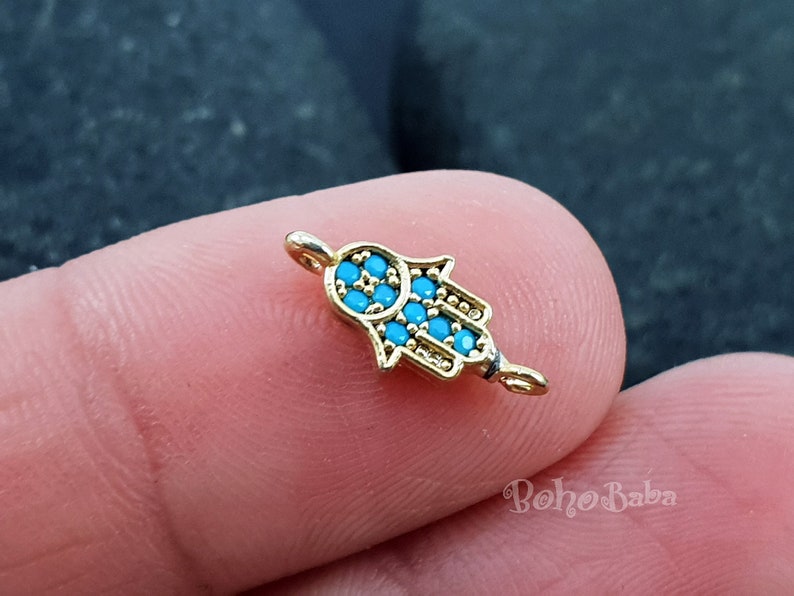 Puede incluir: Encanto de tono dorado con un dise&ntilde;o de mano de hamsa azul. El encanto tiene un peque&ntilde;o bucle en la parte superior para sujetarlo a joyas.