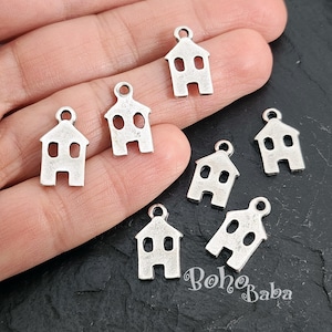 May include: A close-up of seven silver charm pendants shaped like houses. The charms have a simple design with two windows and a door.