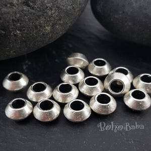 May include: A close-up of a group of silver metal beads. The beads are round and have a hole in the center. They are arranged in a random pattern on a black surface.