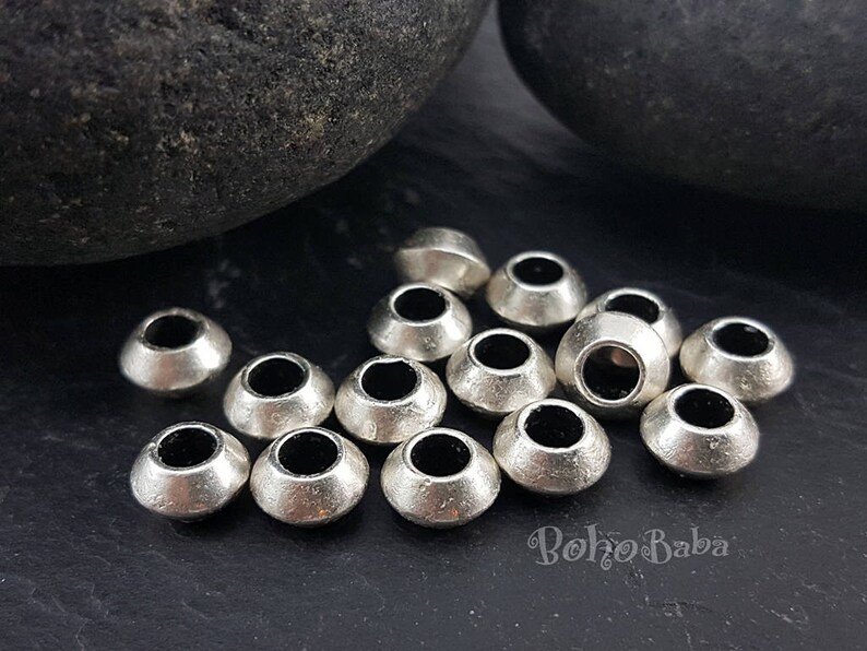 May include: A close-up of a group of silver metal beads. The beads are round and have a hole in the center. They are arranged in a random pattern on a black surface.