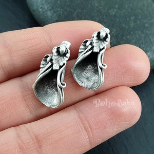 Pode incluir: Um par de brincos prateados com um design floral. Os brincos têm a forma de uma trombeta ou um chifre.