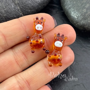 Puede incluir: Dos pequeñas figuritas de jirafa de vidrio con detalles marrones y blancos. Las jirafas están sentadas en una mano.