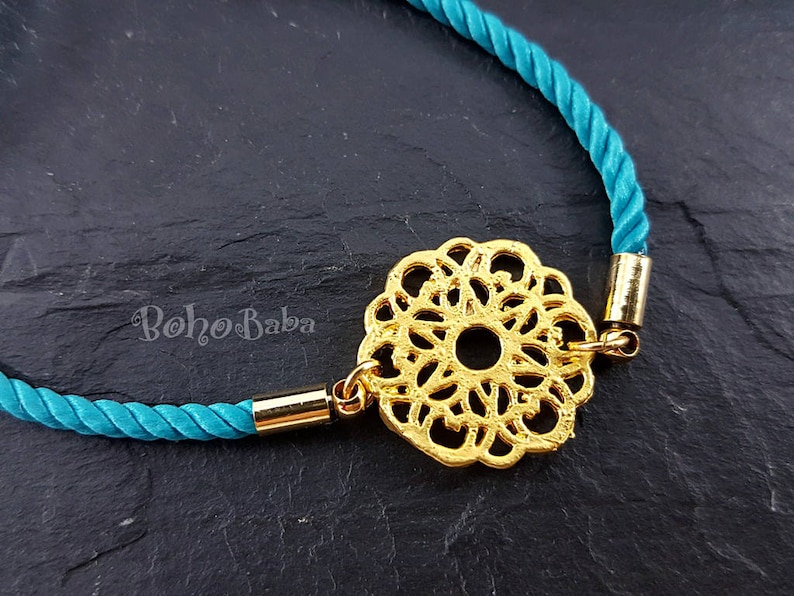 May include: A turquoise cord bracelet with a gold filigree charm. The charm is a circular design with a center hole.