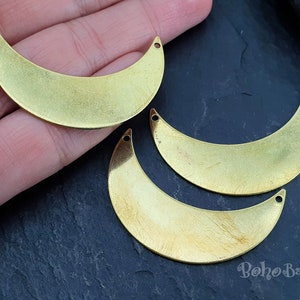 May include: Three gold metal crescent moon shapes with holes at the top for hanging. The moon shapes are on a dark gray surface.