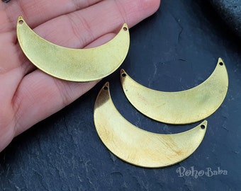 May include: Three gold metal crescent moon shapes with holes at the top for hanging. The moon shapes are on a dark gray surface.