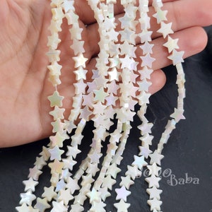 May include: A strand of white iridescent star-shaped beads. The beads are made of mother of pearl and have a slightly irregular shape.