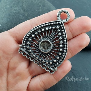 Pu&ograve; includere: Ciondolo in argento con un design decorativo e ornato. Il ciondolo ha un'apertura circolare al centro e un anello nella parte superiore per attaccare una catena.