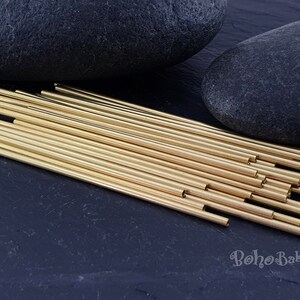 May include: A bundle of 25 gold brass tubes, approximately 6 inches long, arranged in a fan shape on a black surface. The tubes are smooth and shiny, with a slightly rounded edge.