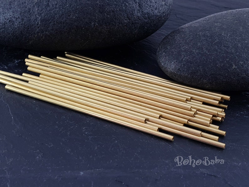 May include: A bundle of 25 gold brass tubes, approximately 6 inches long, arranged in a fan shape on a black surface. The tubes are smooth and shiny, with a slightly rounded edge.