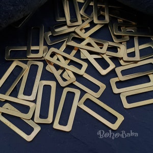 May include: A large pile of gold-coloured metal rectangular rings with a small opening in the centre. The rings are scattered on a dark blue surface.