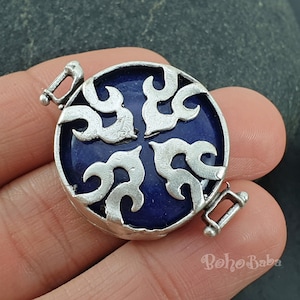 Puede incluir: Cierre de tono plateado con una incrustación de esmalte azul con un diseño floral decorativo. El cierre es redondo y tiene dos bucles a cada lado.