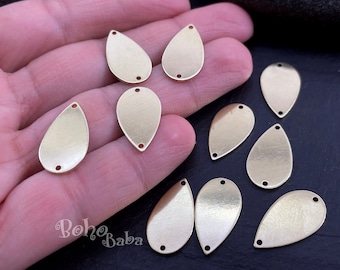 May include: A collection of ten gold-toned metal teardrop-shaped charms with two holes each. The charms are arranged on a hand and a black surface.
