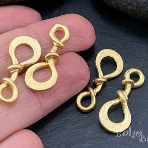 May include: Two pairs of gold-toned metal clasps with a twisted design. Each clasp has two loops, one larger than the other.